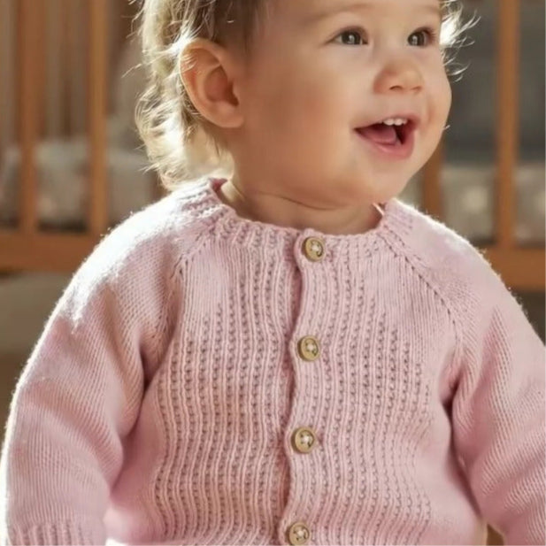 Child wearing a pink knitted cardigan with gold buttons indoors.