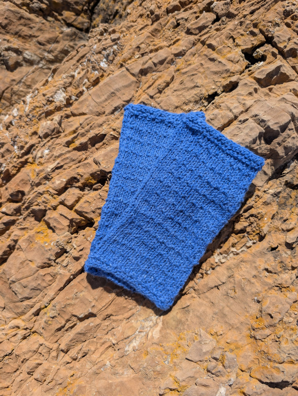 Pair of Jaipur knitted wrist warmers in blue laid flat on red rock